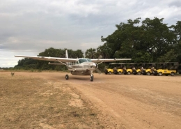 A Cessna Grand Caravan turboprop on an unpaved runway in Selous Game Reserve with Paradise & Wilderness Safari cars waiting