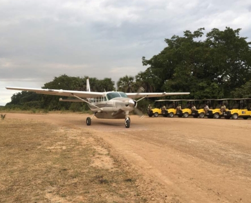 A Cessna Grand Caravan turboprop on an unpaved runway in Selous Game Reserve with Paradise & Wilderness Safari cars waiting