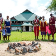Several Maasai dressed in their traditional colorful shukas pose in front of the main building of Africa Safari Serengeti Ikoma